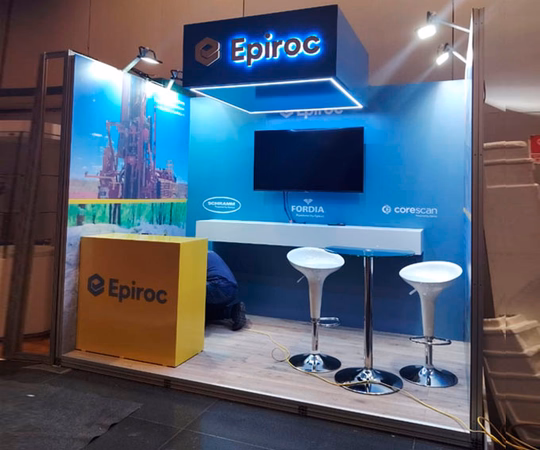 展示台上印有Epiroc品牌，两把白色吧凳，一个黄色柜台，墙上挂着的屏幕，背景有宣传图案。