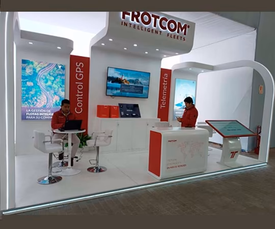 两个人在Frotcom的一个展台工作，展台上展示了远程信息处理和GPS控制解决方案，包括显示器、宣传册和品牌资料。