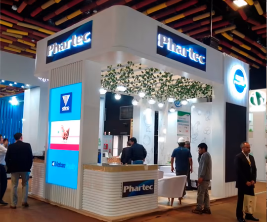 Phar-tec展会展台设有发光招牌、数字展示、座位区，以及几位站立和走动的观众。